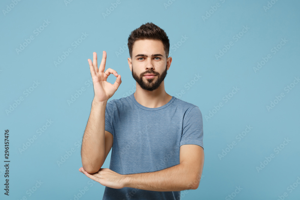 Fototapeta premium Young attractive handsome man in casual clothes posing isolated on blue background, studio portrait. People sincere emotions lifestyle concept. Mock up copy space. Looking camera, showing OK gesture.
