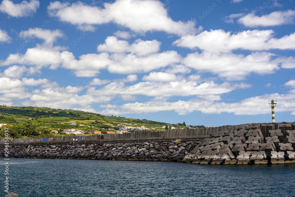 Portugal, San Miguel, June 2019. White fluffy clouds in the blue sky, lighthouse and marina of Vila Franca do Campo, Azores. Amazing ride. Portugal, San Miguel, June 2019. White fluffy clouds in the blue sky, lighthouse and marina of Vila Franca do Campo, Azores. Amazing ride.