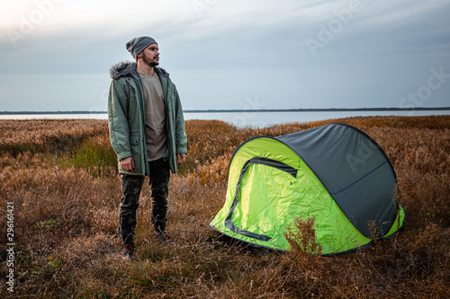 A bearded man near a camping tent in green on the background of nature and the lake. The concept of travel  tourism  camping.