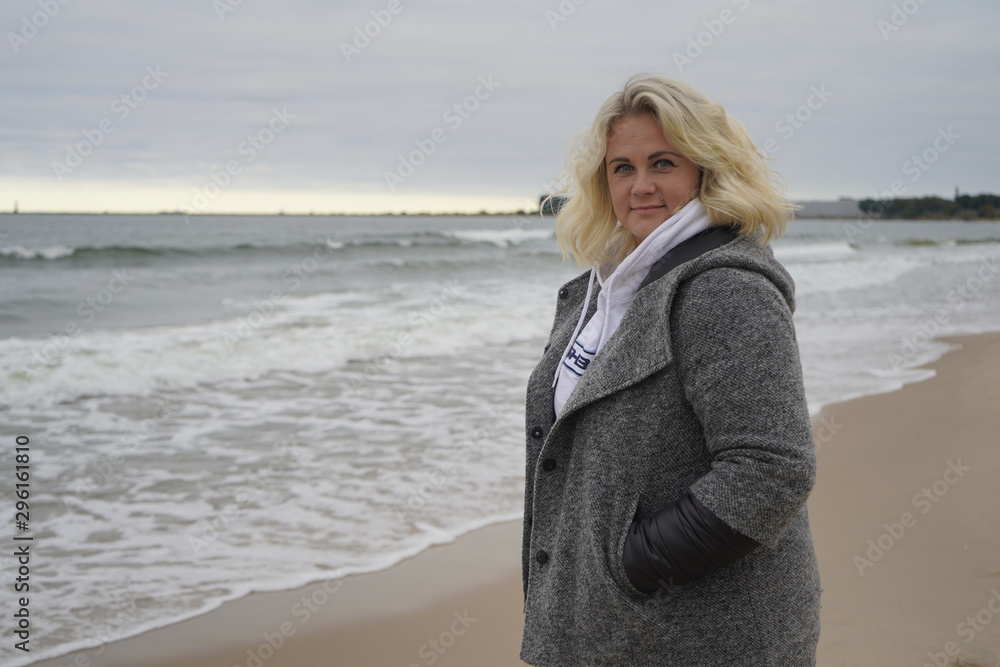 The girl turns and looks into the camera lens on the background of the cold sea. Blond hair in the wind. Hair and sea breeze. close-up The girl turns and looks into the camera lens on the background of the cold sea. Blond hair in the wind. Hair and sea breeze. close-up