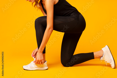 Unrecognizable Lady Lacing Shoes Over Yellow Studio Background, Cropped photo