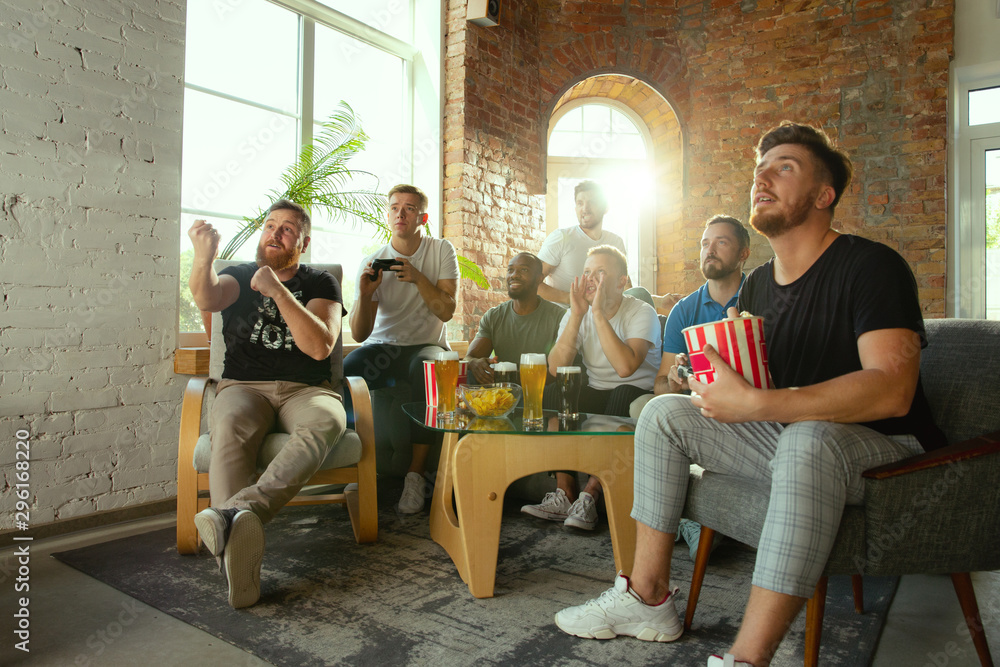 Group of excited friends playing video games at home. Caucasian male gamers or fans spending time and having fun together at home. Emotional watching gameplay. Modern technologies, friendship, weekend Group of excited friends playing video games at home. Caucasian male gamers or fans spending time and having fun together at home. Emotional watching gameplay. Modern technologies, friendship, weekend