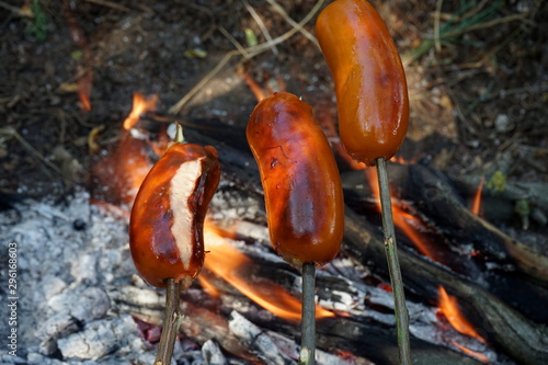 Sausages on homemade wooden skewers are fried on a fire during a picnic