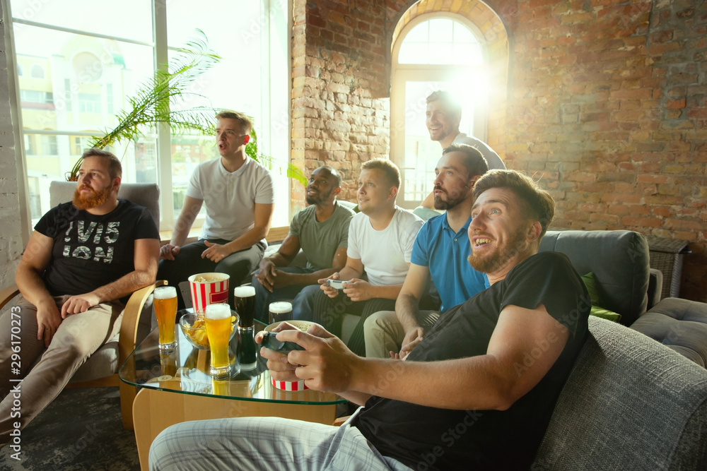Group of excited friends playing video games at home. Caucasian male gamers or fans spending time and having fun together at home. Emotional watching gameplay. Modern technologies, friendship, weekend Group of excited friends playing video games at home. Caucasian male gamers or fans spending time and having fun together at home. Emotional watching gameplay. Modern technologies, friendship, weekend