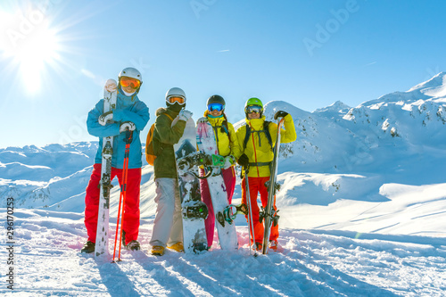 Four happy friends snowboarders and skiers are having fun on ski slope with ski and snowboards in sunny day.