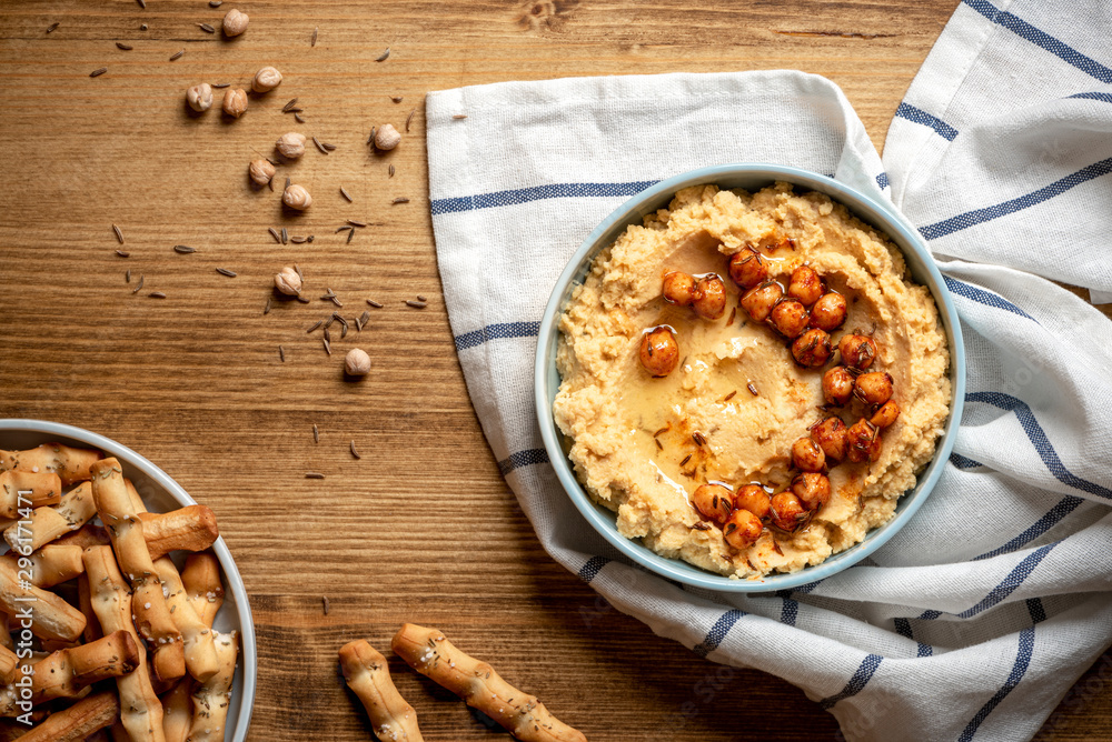 Hummus with olive oil and chickpeas in a ceramic plate on a wooden background, top view. Traditional middle eastern snack hummus, healthy vegetarian food. Hummus with olive oil and chickpeas in a ceramic plate on a wooden background, top view. Traditional middle eastern snack hummus, healthy vegetarian food.