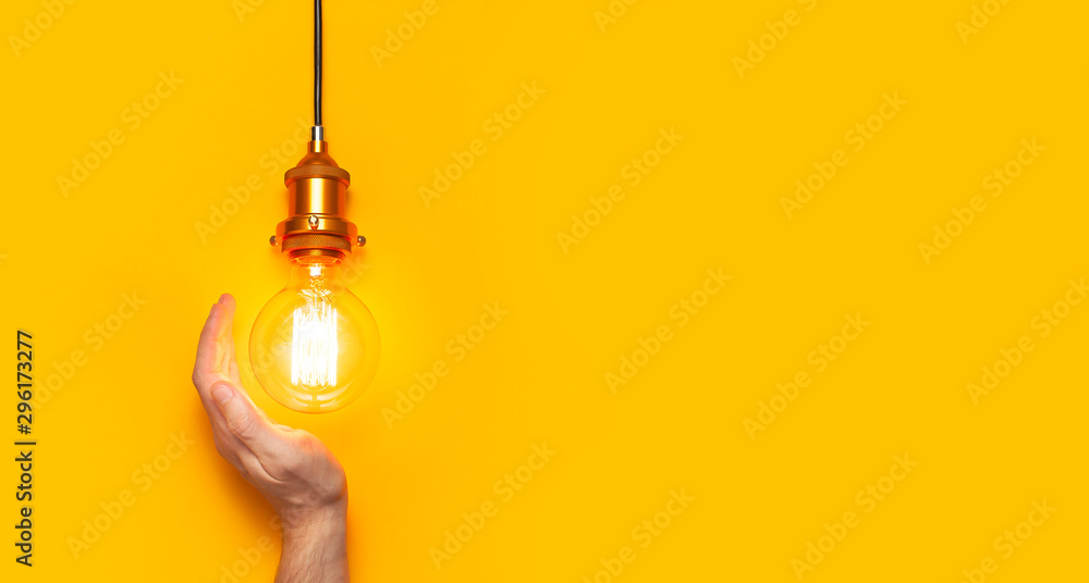 Vintage fashionable edison lamp in male hands on bright yellow background. Top view flat lay copy space. Creative idea concept, designer lamp, modern interior item. Lighting, electricity - obrazy, fototapety, plakaty 