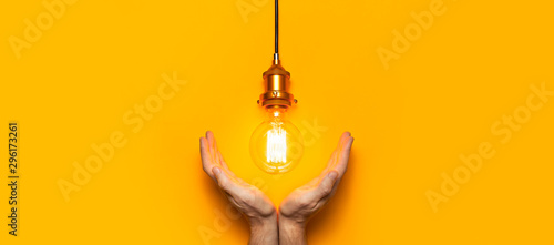 Vintage fashionable edison lamp in male hands on bright yellow background. Top view flat lay copy space. Creative idea concept, designer lamp, modern interior item. Lighting, electricity