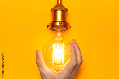 Vintage fashionable edison lamp in male hands on bright yellow background. Top view flat lay copy space. Creative idea concept, designer lamp, modern interior item. Lighting, electricity