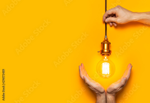 Vintage fashionable edison lamp in male hands on bright yellow background. Top view flat lay copy space. Creative idea concept, designer lamp, modern interior item. Lighting, electricity