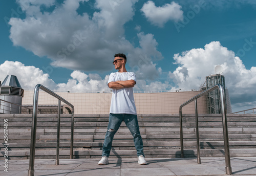 sports guy stands pose break dance dancer, hip-hop summer city background steps clouds. Active youth lifestyle, young male fitness movement workout breakdancer. In t-shirt jeans sneakers, sunglasses.