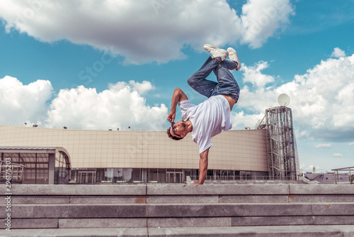 dancer on one arm dances break dance, hip-hop, artist acrobat. Summer city, clouds background. Active youth lifestyle, young male dancer, fitness movement workout breakdancer. Free space for text. photo