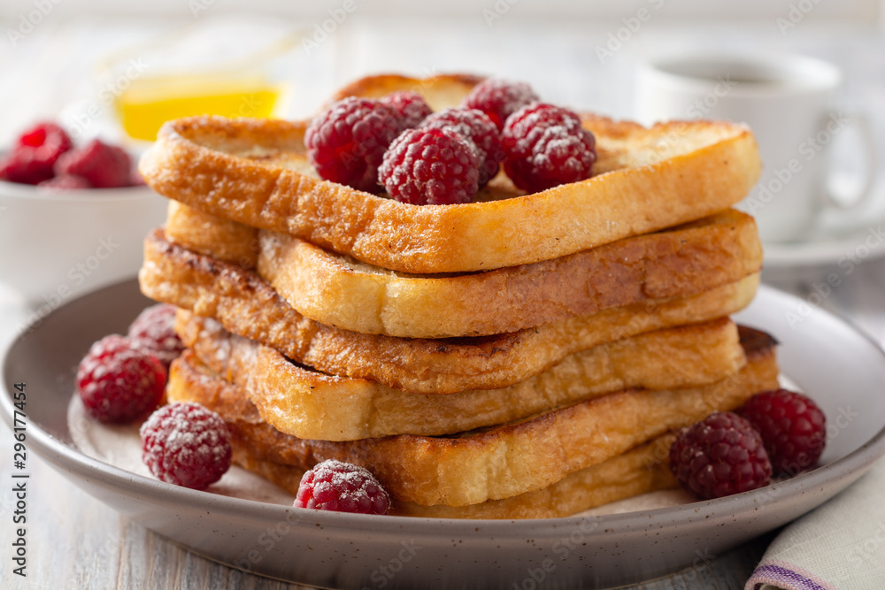 French toasts with powdered sugar and fresh raspberries on wooden table. Selective focus. French toasts with powdered sugar and fresh raspberries on wooden table. Selective focus.