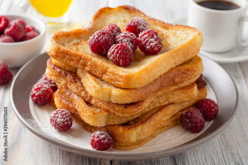 French toasts with powdered sugar and fresh raspberries on wooden table. Selective focus. French toasts with powdered sugar and fresh raspberries on wooden table. Selective focus.