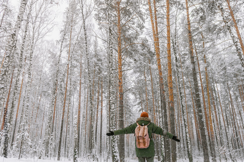 A young man with a red backpack stands in a snowy forest with his arms wide open in a snowy forest. The silence of the winter forest. Winter fairy tale. Christmas mood.