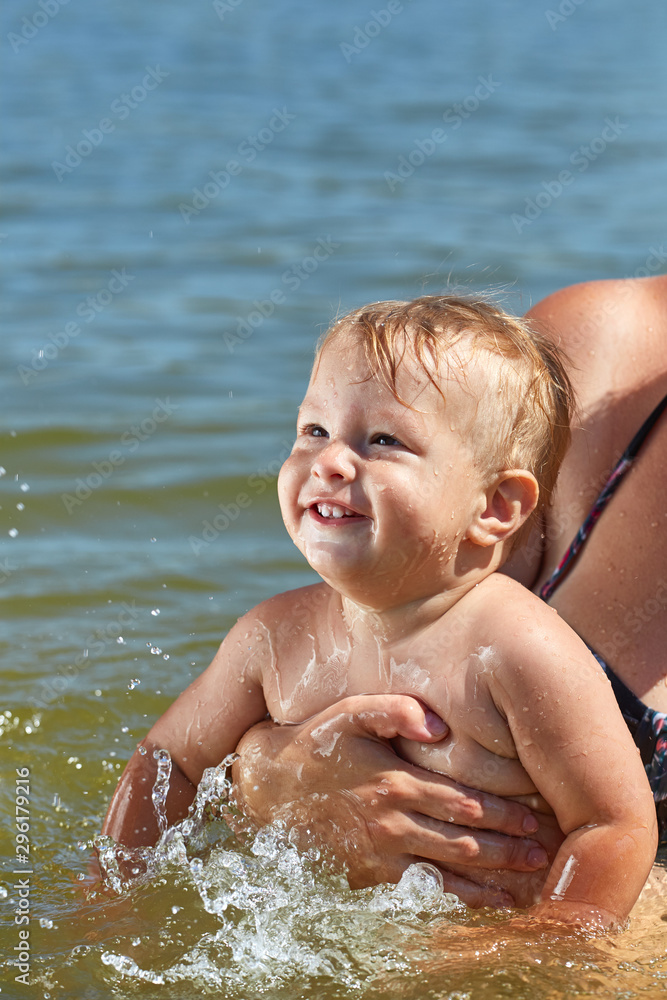 Cheerful cute child bathes in the water in her mother’s arms Cheerful cute child bathes in the water in her mother’s arms