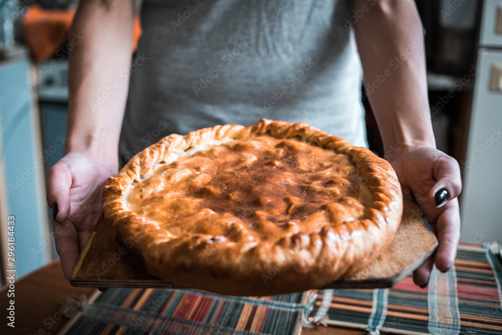 female hands hold a fresh hot apple pie in the kitchen. made with your own hands