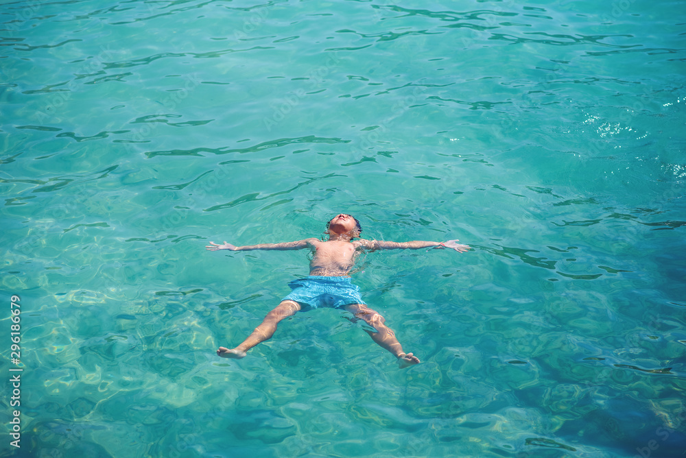 Schoolboy enjoying his summer vacations, he is floating in clear blue water in form of sea star.