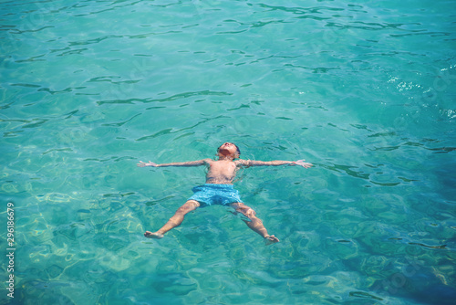 Schoolboy enjoying his summer vacations, he is floating in clear blue water in form of sea star.