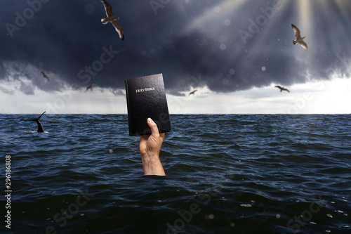 drowning man holding bible into the sky