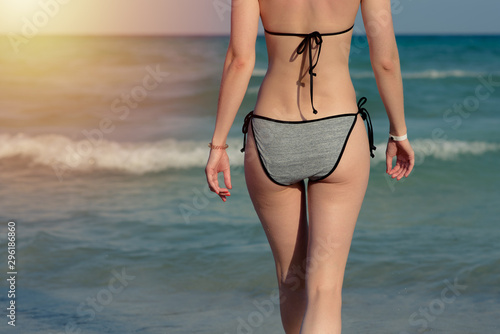 Slender European woman in swim suit on sand beach against sea. Close-up view.