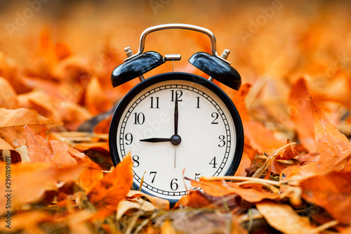Autumn concept. Alarm clock black on a background of yellow fallen foliage. Fall season