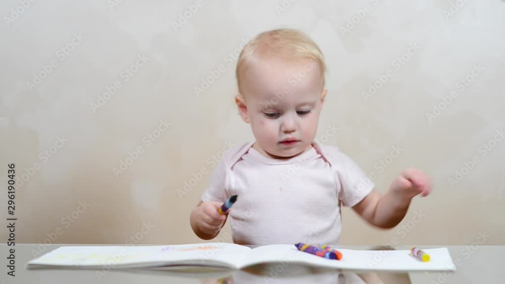 The child draws scribbles in the album and builds funny grimaces The child draws scribbles in the album and builds funny grimaces