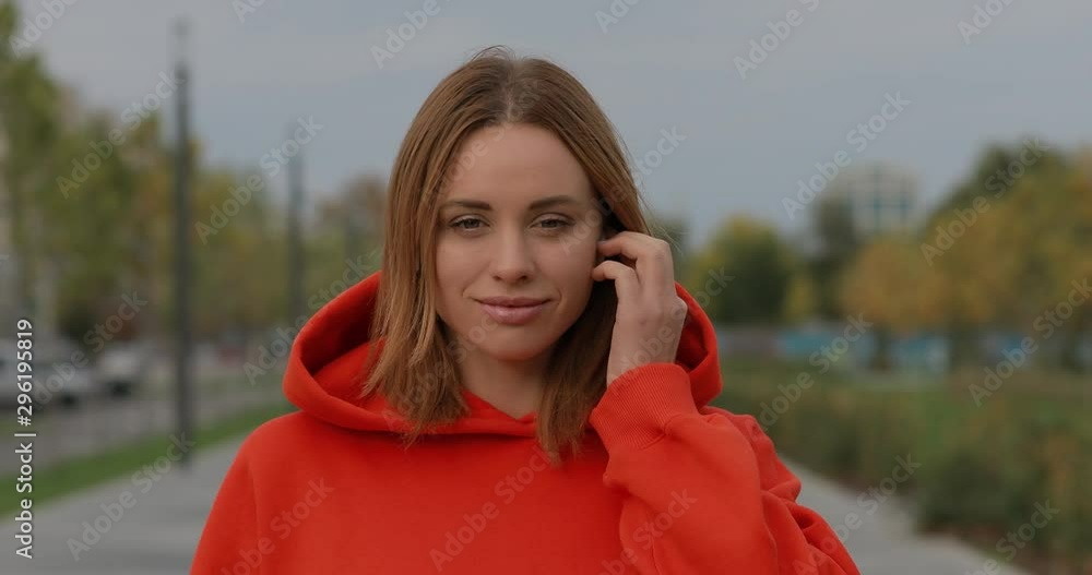 European woman puts on wireless earphones and wear hood in autumn day for listening music European woman puts on wireless earphones and wear hood in autumn day for listening music