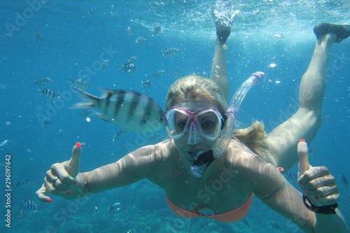 blond woman snorkling in clear water rurrounded with fish