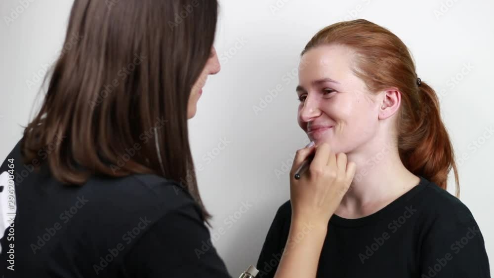 Brown-haired woman doing red-haired girl makeup. Application of a cream. Brown-haired woman doing red-haired girl makeup. Application of a cream.