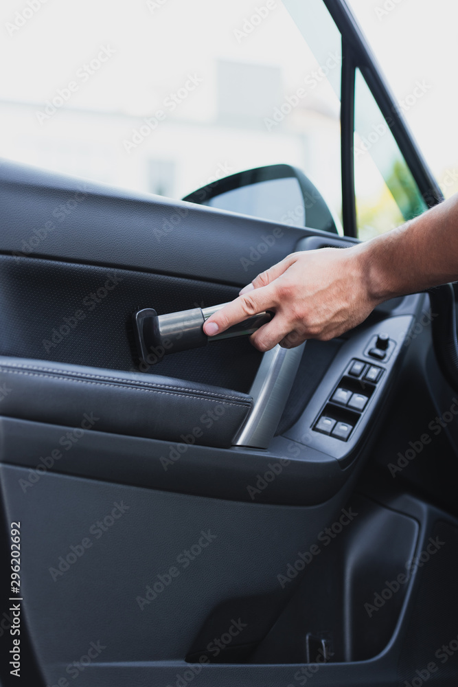 partial view of car cleaner vacuuming car front door