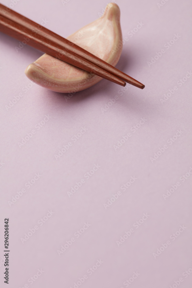 Wooden chopsticks and chopstick rest on bright paper background. Close up. Copy space. Wooden chopsticks and chopstick rest on bright paper background. Close up. Copy space.
