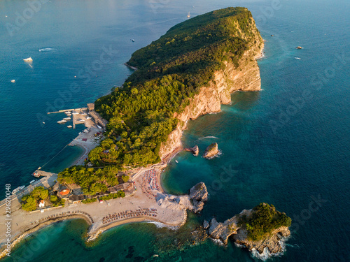 Aerial view of Sveti Nikola, Budva island, Montenegro. Hawaii beach, umbrellas and bathers and crystal clear waters. Jagged coasts with sheer cliffs overlooking the transparent sea. Wild nature
