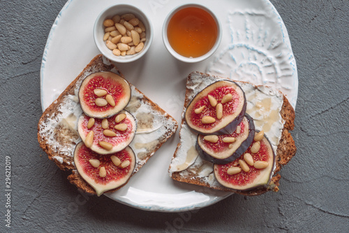 Fig toast with cheese, honey and pine nuts on a white plate. Rustic breakfast or lunch. Pine nuts and honey on a plate top view. 