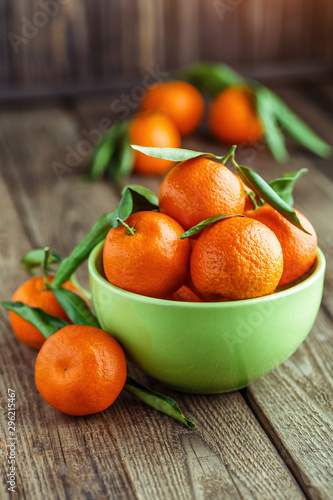 Ripe Mandarin fruit peeled open and place on old rustic look timber with group of mandarin fruits and leaves out of focus on the background