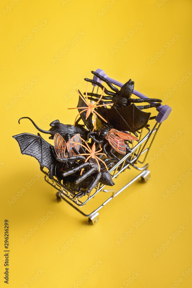 Halloween attributes spider, bat, mouse, fly in the supermarket trolley on the yellow background Halloween attributes spider, bat, mouse, fly in the supermarket trolley on the yellow background