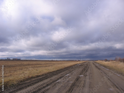 muddy earthen autumn road on a dirt road in a dried up field under overcast clouds