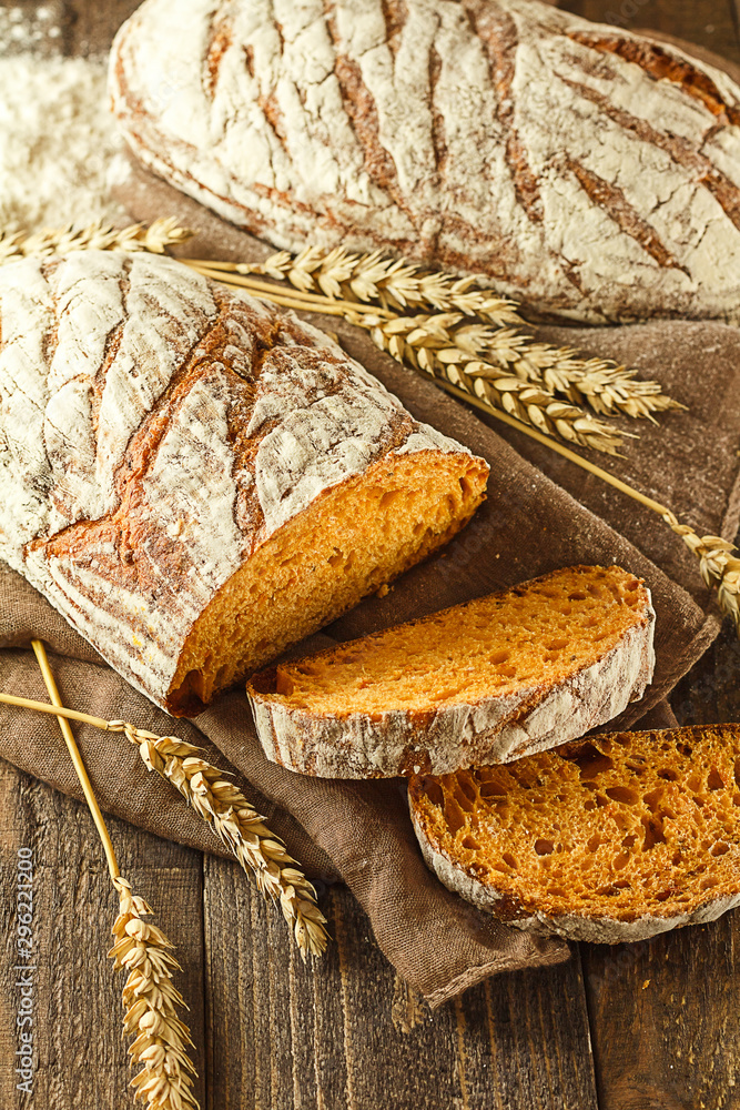 Fresh pumpkin sliced bread on a dark wooden background with whole bread and wheat in the background