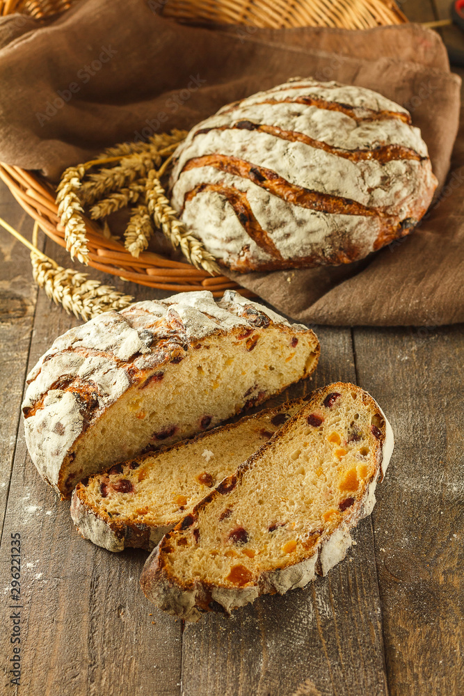 Fresh sliced bread on a dark wooden background with whole bread and wheat in the background