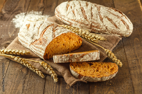 Fresh pumpkin sliced bread on a dark wooden background with whole bread and wheat in the background