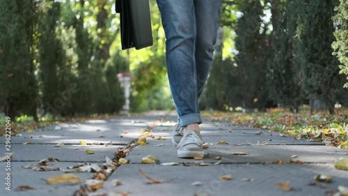 Attractive young business woman with a briefcase in a black jacket and glasses steps, walks and dances outdoors. Rejoices, laughs and has fun in the park. Closeup feet and face. Dancing in park.