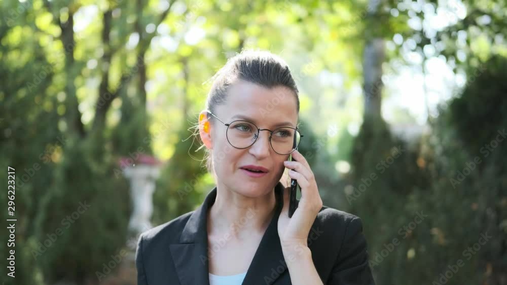 Attractive young business woman with briefcase in black jacket and glasses steps, walks and dances outdoors. Speaks on phone and laughs. Close-up of legs and head. Autumn park, yellow leaves. Attractive young business woman with briefcase in black jacket and glasses steps, walks and dances outdoors. Speaks on phone and laughs. Close-up of legs and head. Autumn park, yellow leaves.