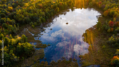 aerial perspective. sunset on pond with sun streaks cascading in photo reflections on pond with beaver hut 