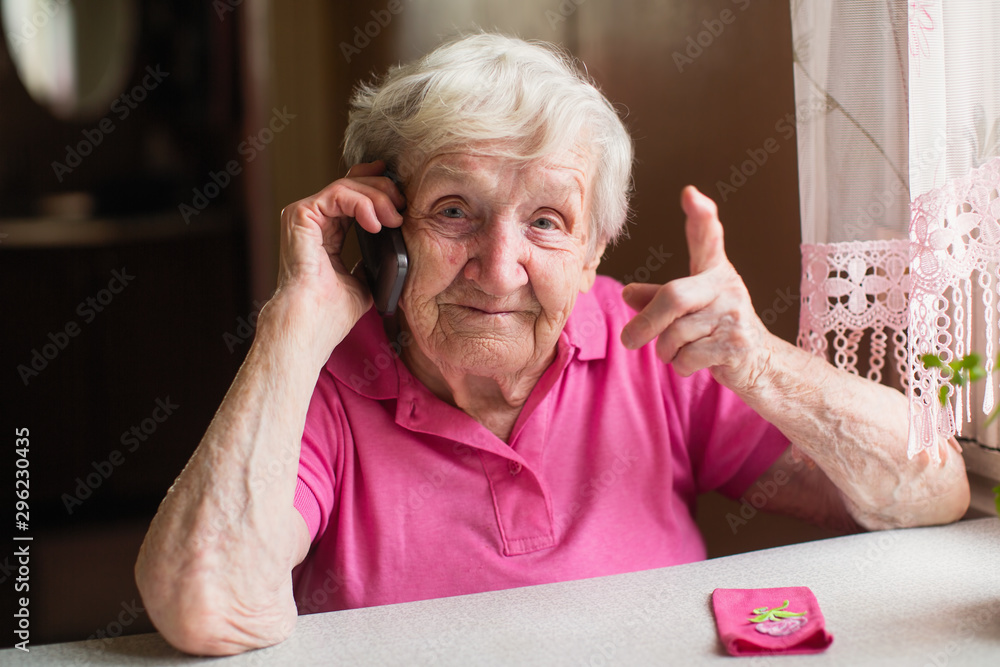 An elderly woman talks on a mobile phone sitting at his home.