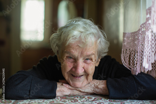 Close-up portrait of an old gray-haired woman sitting at a table in the house.