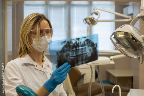 Woman dentist in dental office stares at x-ray image of tooths. photo