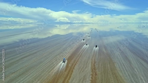 Aerial of four wheel drive vehicles cross the flooded Salar de Uyuni, world's largest salt flat, near Daniel Campos Province, Bolivia. Drone slow tracking shot