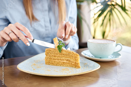 Honey sponge cake decorated with meringue and mint leaves. A young woman drinks coffee cappuccino in a restaurant and eats dessert. Breakfast in the cafe, morning coffee. Restaurant menu