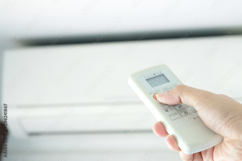 Fototapeta premium Man's hand using remote control open The air conditioner is cooled to 25 degrees Celsius in his bedroom. Health concepts and energy savings