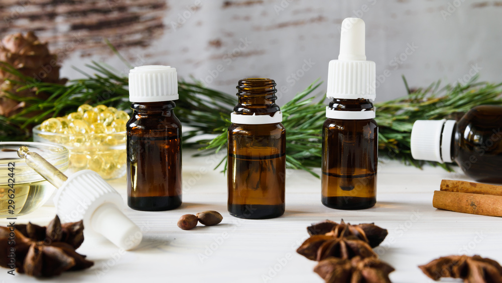 composition of natural oils, glass bottles with oil, cinnamon sticks, anise, pine nuts on a white wooden table on a background of green branches